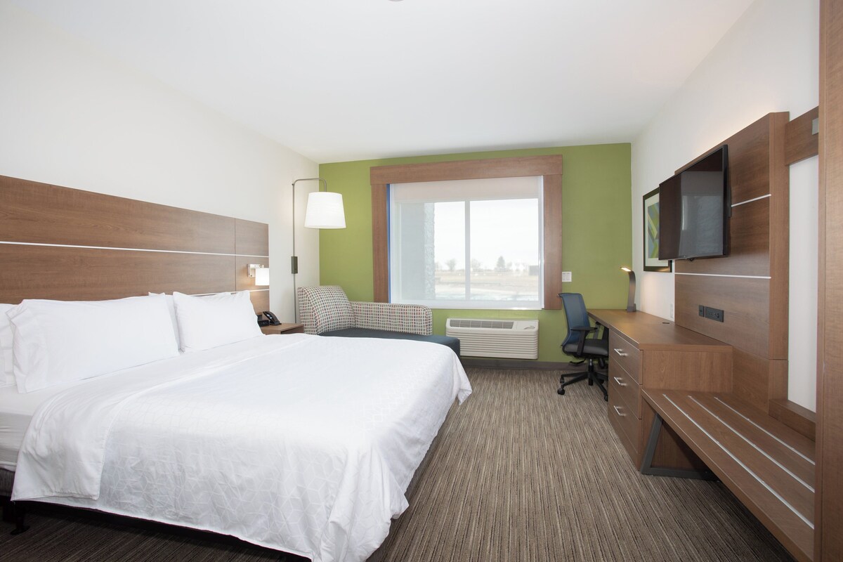 A hotel room with a large bed, a desk, a chair, a television, and a window with a view.