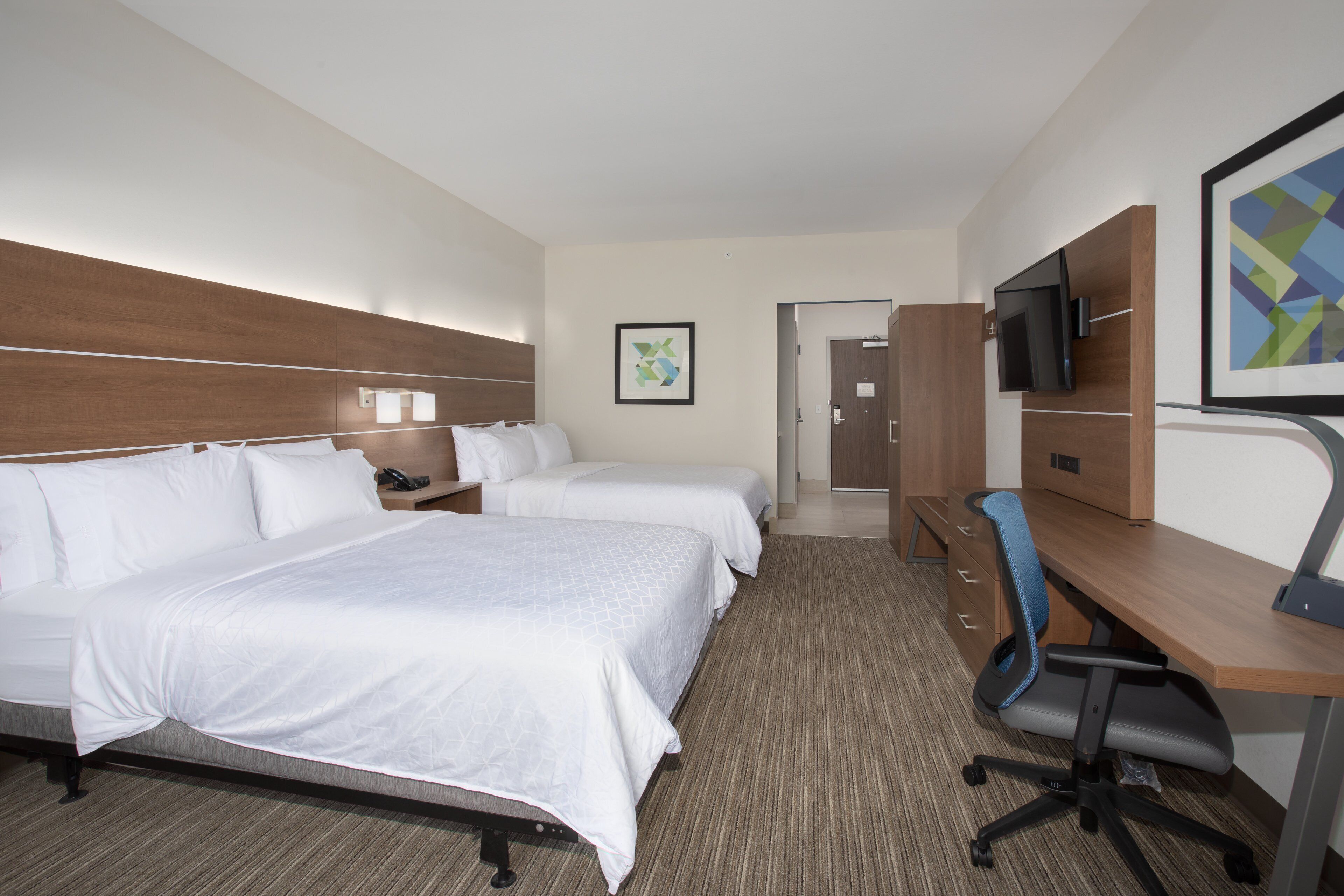 A hotel room with two beds, a desk, a chair, a TV, and a framed picture on the wall.