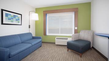 Ein Zimmer mit einem blauen Sofa, einem gemusterten Sessel, einem großen Fenster und einem gerahmten Bild an der Wand.