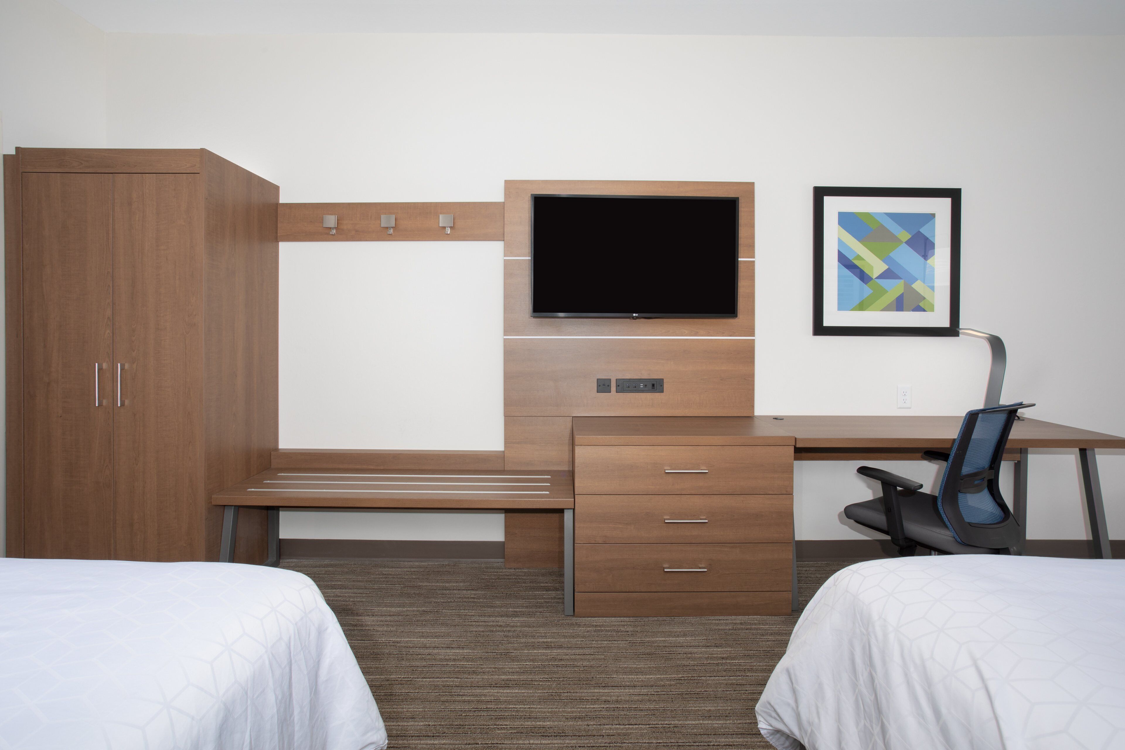 Une chambre d’hôtel avec un bureau en bois, un téléviseur à écran plat, une chaise, deux lits et un tableau encadré au mur.