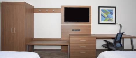 Habitación de hotel con un escritorio de madera, un televisor de pantalla plana, una silla, dos camas y un cuadro en la pared.