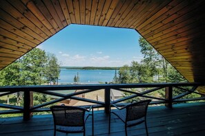 Um deck de madeira com duas cadeiras de frente para um lago e colinas arborizadas.