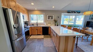 Une cuisine moderne avec des meubles en bois, des appareils électroménagers en acier inoxydable, un îlot central et de grandes fenêtres.
