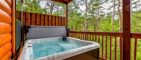 A hot tub on a wooden deck with a view of a forest.