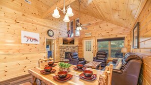 A wooden cabin interior with a dining table set with bowls, two leather sofas, and a fireplace. - Free Tickets | Hot Tub, Pool Table, Media Room, Easy Access Crazy Like a Fox! (Pigeon Forge)