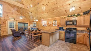 A log cabin interior with a wooden ceiling, a kitchen with a stove and microwave, a dining area with a bench, and a fireplace. - Free Tickets | Hot Tub, Pool Table, Media Room, Easy Access Crazy Like a Fox! (Pigeon Forge)