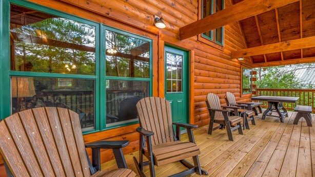 A wooden cabin with a porch featuring Adirondack chairs, a table, and a bench. - Free Tickets | Hot Tub, Pool Table, Media Room, Easy Access Crazy Like a Fox! (Pigeon Forge)