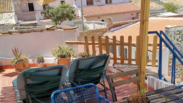 A terrace with wooden tables and chairs, potted plants, and a view of buildings in the background. - Village house with large terrace.  (Valencia)