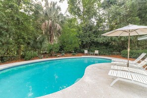 A swimming pool with white lounge chairs and an umbrella, surrounded by lush greenery. - DOG FRIENDLY Four Bedroom 3rd Row Ocean Sea Pines Home with a Private Pool (Hilton Head Island)