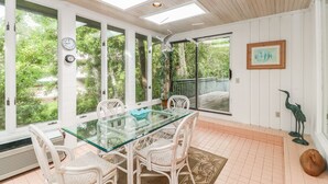 A sunroom with a glass table and chairs, large windows, and a view of greenery. - DOG FRIENDLY Four Bedroom 3rd Row Ocean Sea Pines Home with a Private Pool (Hilton Head Island)