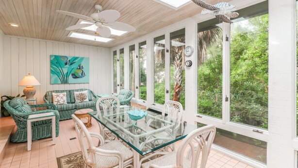 A sunlit room with a glass table, wicker furniture, and a view of lush greenery. - DOG FRIENDLY Four Bedroom 3rd Row Ocean Sea Pines Home with a Private Pool (Hilton Head Island)