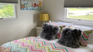 A bedroom with a bed, pillows, a lamp, a painting, and a window with blinds.