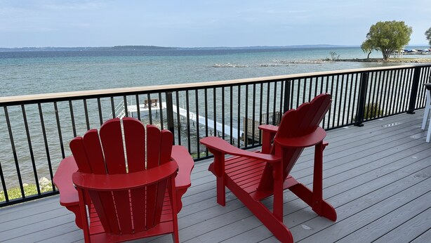 A wooden deck with two red Adirondack chairs facing a body of water.