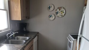 A kitchen with wooden cabinets, a granite countertop, a plaid rug, a coffee maker, and a refrigerator.