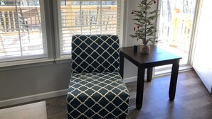 Ein Zimmer mit einem gemusterten Sessel, einem kleinen Tisch mit Weihnachtsbaum und Blick durch große Fenster.