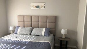 Ein Schlafzimmer mit einer gesteppten Kopfteil, einem Bett mit einem gemusterten Überwurf, zwei Nachttischen mit Lampen und einem Wandbild.