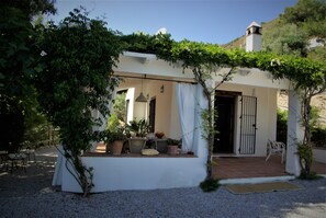 A white building with a covered patio area, potted plants, and a small seating area. - Sainte Fontaine. Country house in Frigiliana, with views of the sea and the mountains. (Frigiliana)