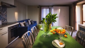 Ein Essbereich mit grüner Tischdecke, einer Vase mit Grünpflanzen und einer Orangenschale.