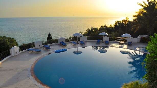 A circular infinity pool with lounge chairs and umbrellas, overlooking a body of water at sunset. - Studio mit Pool Maria am Agios Gordios (Agios Gordios)