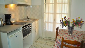A small kitchen with a coffee maker, oven, and sink. There's a dining table with a floral tablecloth and a vase of flowers. - Studio mit Pool Maria am Agios Gordios (Agios Gordios)