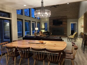 A spacious dining area with a large wooden table and chairs, a fireplace, and a seating area with sofas and chairs.
