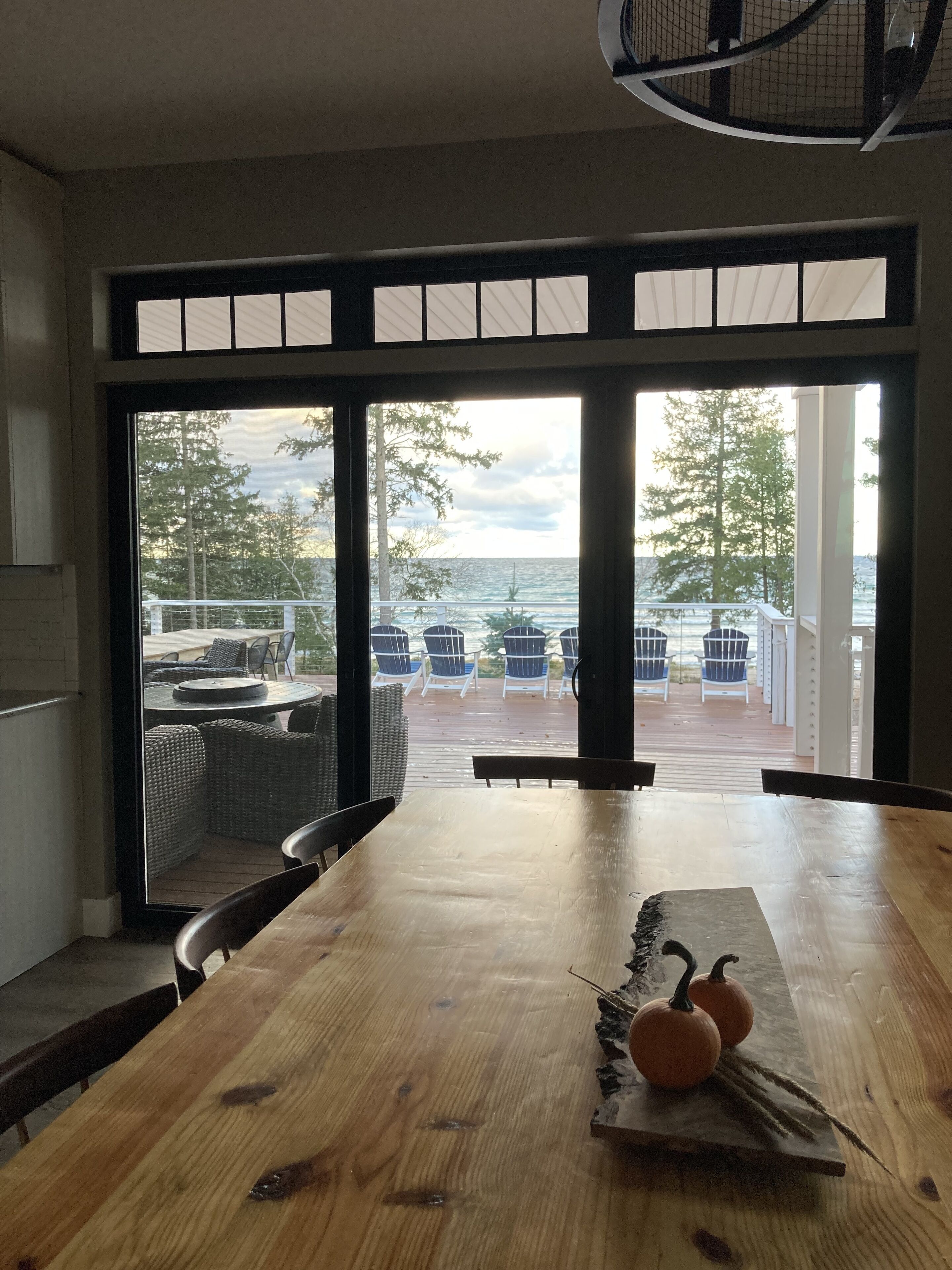 A wooden dining table with chairs, a view of the ocean, and outdoor seating with chairs and a table.