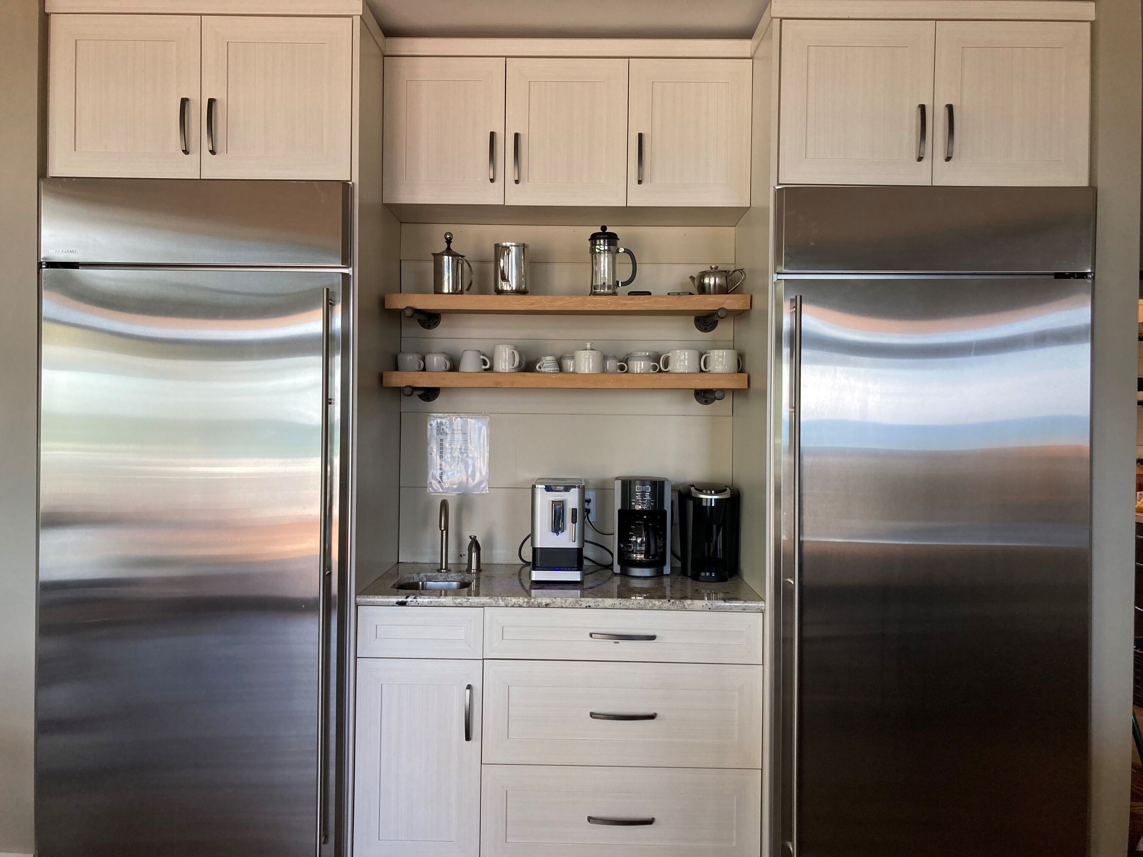 A modern kitchen with stainless steel appliances, wooden shelves, and a coffee maker.