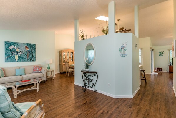 A spacious living room with hardwood floors, a sofa, a coffee table, and a dining area in the background.