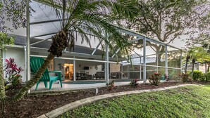 A modern house with a glass conservatory, green outdoor seating, and a well-maintained garden. - Jumpin Fish House 3BR/2BA Pool Home on the Canal (Sebastian)