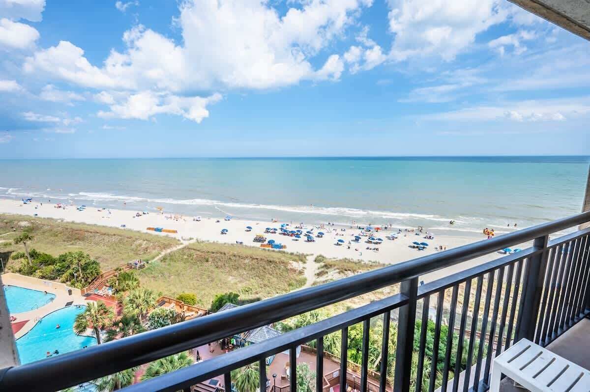 Une vue sur la plage depuis un balcon, avec une piscine et un ciel dégagé.