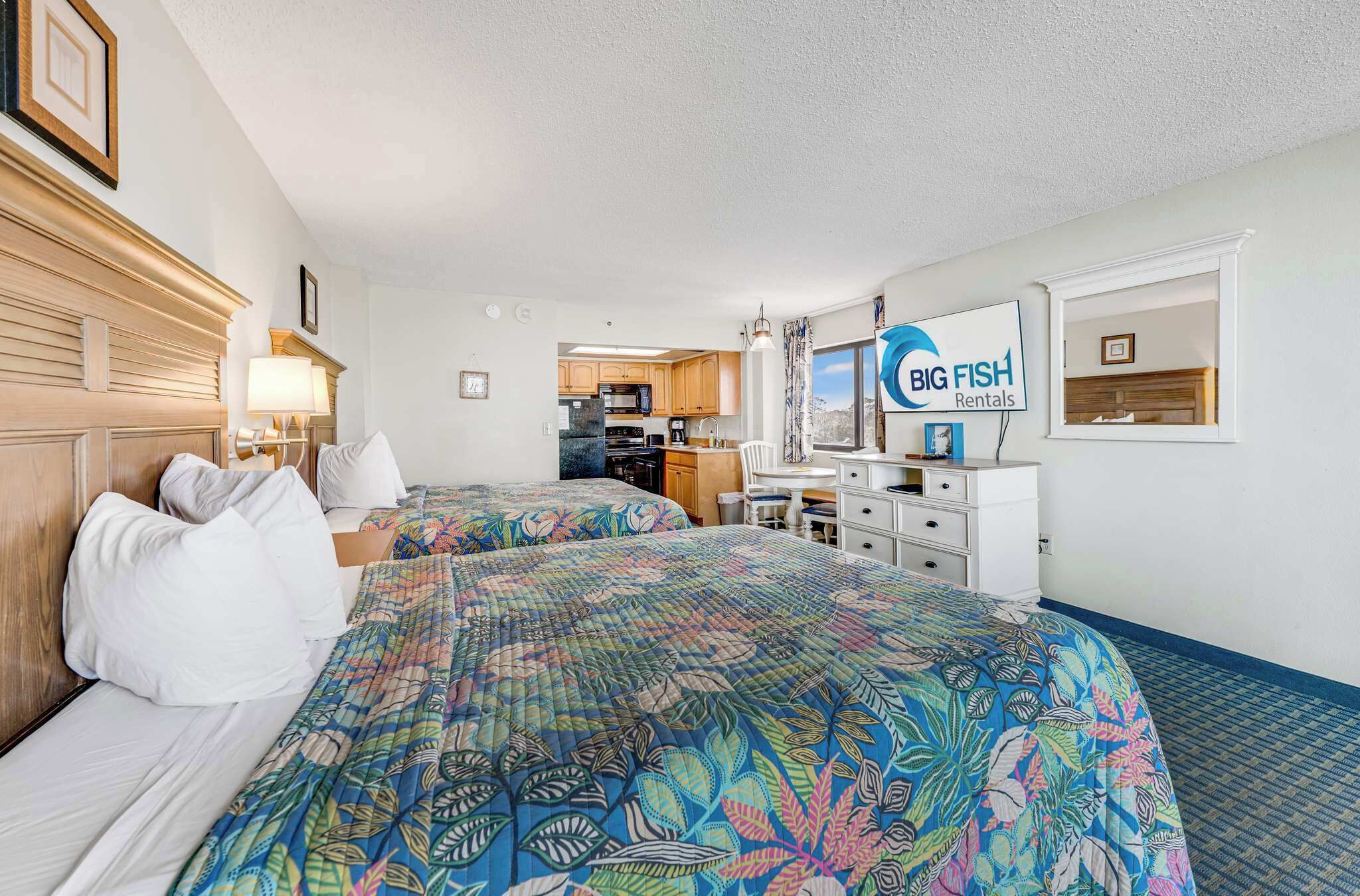 A hotel room with two beds, a kitchenette, a dining area, and a view of the ocean.