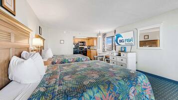 A hotel room with two beds, a kitchenette, a dining area, and a view of the ocean.