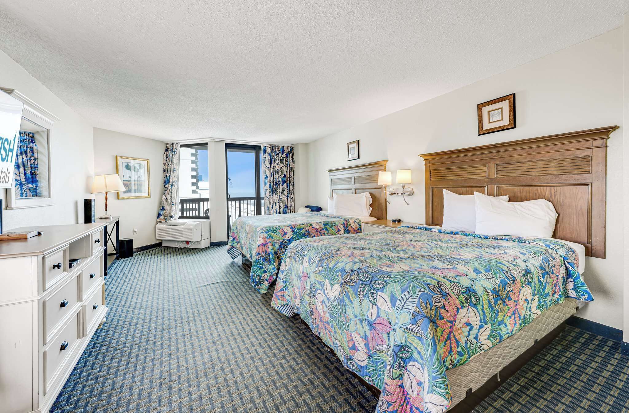 A hotel room with two beds, a dresser, a vanity, a window with a view, and a balcony.