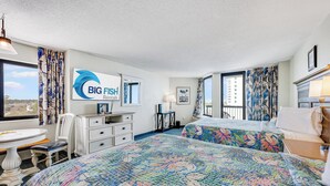 A hotel room with a large bed, a desk, and a chair. There is a sign on the wall that reads "BIG FISH Rentals." - Oceanview Studio at Compass Cove with Pools,Updated! (Myrtle Beach)