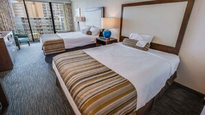 A hotel room with two beds, a desk, and a large window with a view of other buildings.