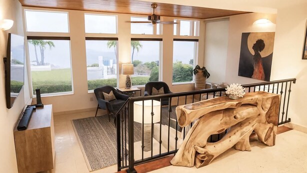 Amplia sala de estar con ventanas grandes, una mesa de centro de madera y una escalera moderna.