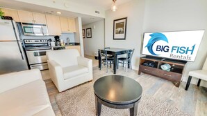 Una cocina moderna con electrodomésticos de acero inoxidable, una zona de comedor con mesa y sillas, y un televisor de pantalla plana sobre un mueble de madera.