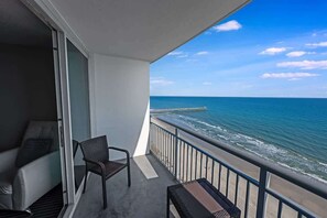 Un balcon avec vue sur l’océan et sur une jetée. On y trouve une chaise et une petite table.