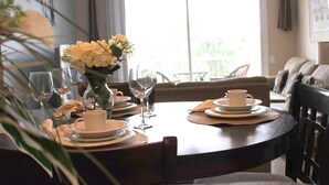 A dining table set with plates, glasses, and a vase of flowers, with a view of a balcony and a sofa in the background. - Windsor_palms_303cp-n (Kissimmee)