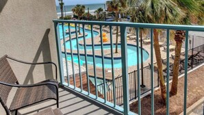 Un balcón con vista a un área de piscina, que incluye una piscina sinuosa y palmeras.