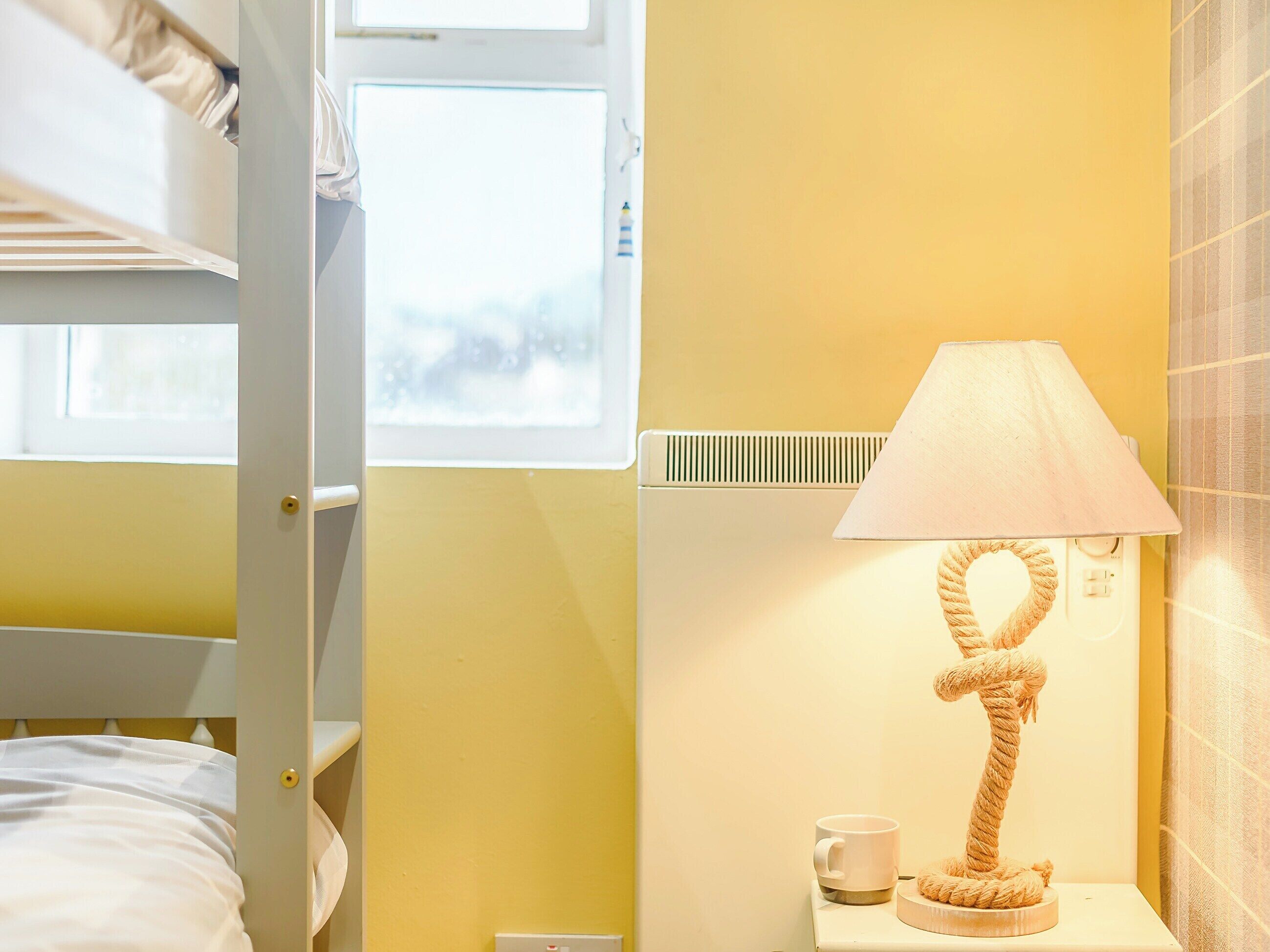 Ett hotellrum med en våningssäng, en sänglampa, en kopp och ett fönster.