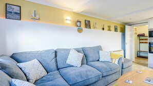 A living room with a sofa, cushions, a coffee table, a wall clock, and a shelf with decorative items.