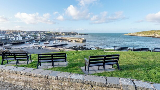 A coastal town with a marina, benches on a grassy area, and a clear view of the sea.