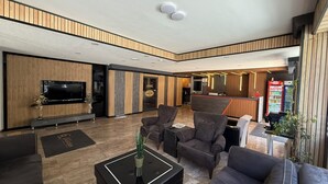 Un moderno vestíbulo de hotel con televisor de pantalla plana, asientos cómodos, mostrador de recepción y un refrigerador Coca-Cola.