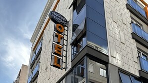 Un hotel moderno con un cartel llamativo que dice "COMFORT BASARAN HOTEL" y "OTEL COMFORT". Presenta una construcción de varios pisos con grandes ventanales y un área de balcón.