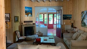 Een gezellige woonkamer met een open haard, een bank, een bijzettafeltje en een deur naar een zonnig terras.