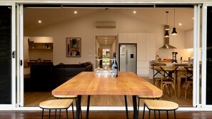 Un intérieur moderne comprenant une table à manger en bois, des chaises, un coin cuisine et un salon avec un canapé et un tableau.
