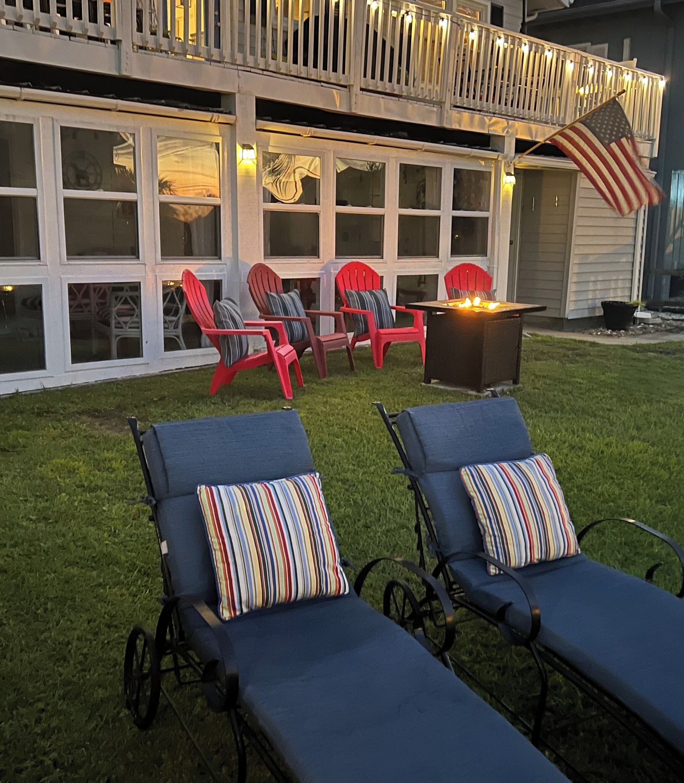 Un jardin avec deux chaises longues, un foyer et des chaises Adirondack rouges.