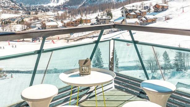 A terrace with a clear view of a snowy mountain landscape, a glass balustrade, and three white stools. - Top floor Apartment, amazing view, on the slopes ! (Val-d'Isère)