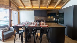 A modern kitchen with a central island, black bar stools, and a dining table set for six. - Top floor Apartment, amazing view, on the slopes ! (Val-d'Isère)